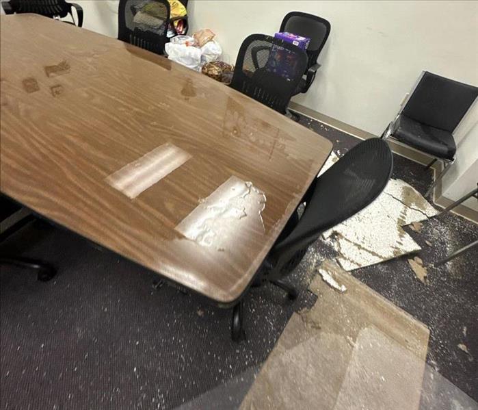 Water damage in a conference room with table and chairs and ceiling debris from damage